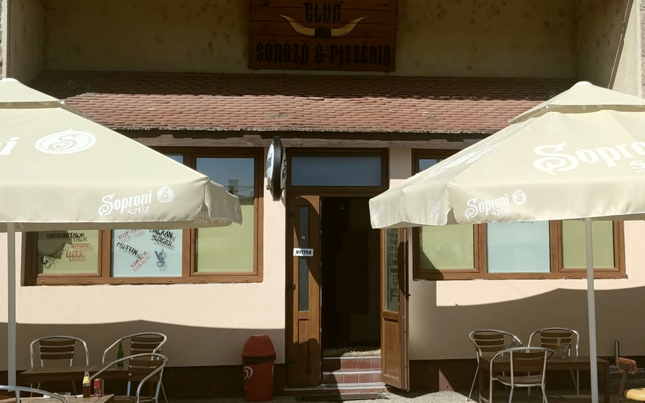 A Western Söröző és Pizzéria bejárata Újszilváson: fatábla cégér, nyitott ajtó, két napernyő és kinti asztalok.