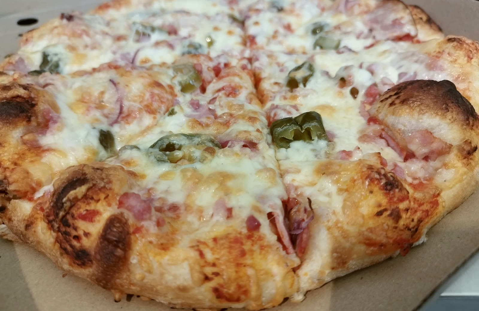 Frissen sült, vékonytésztás pizza a dobozban, sonkával, hagymával és csemegeuborkával, a Western Söröző és Pizzéria Facebook-oldaláról.